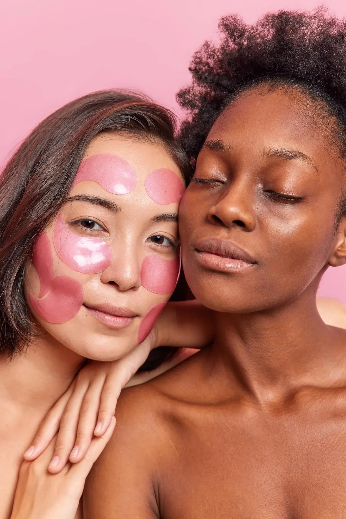 Two women with glowing skin against pink background, one applying pink hydrogel face patches
